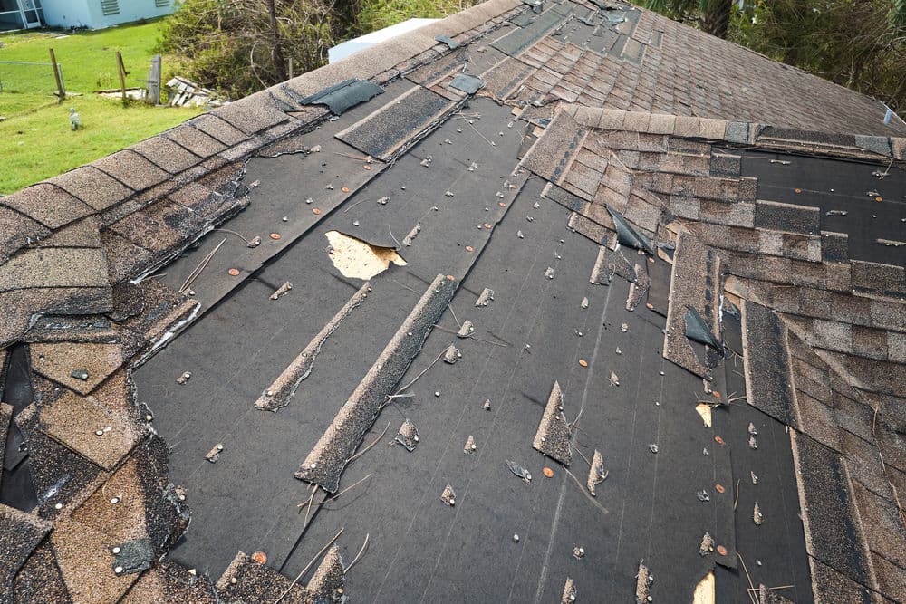 Damaged asphalt shingles on a rooftop with exposed underlayment and debris scattered.