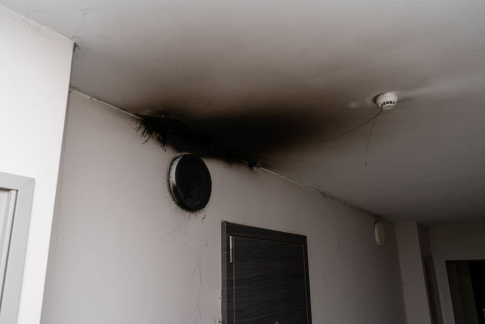 Ceiling damage with soot marks, smoke detector, and door frame in a residential interior.